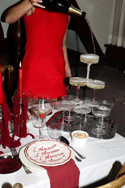 Chez Jules table styling by Imaginary Friends – champagne tower, red candles, L’Amour plate and deep red dinner details on a white tablecloth.