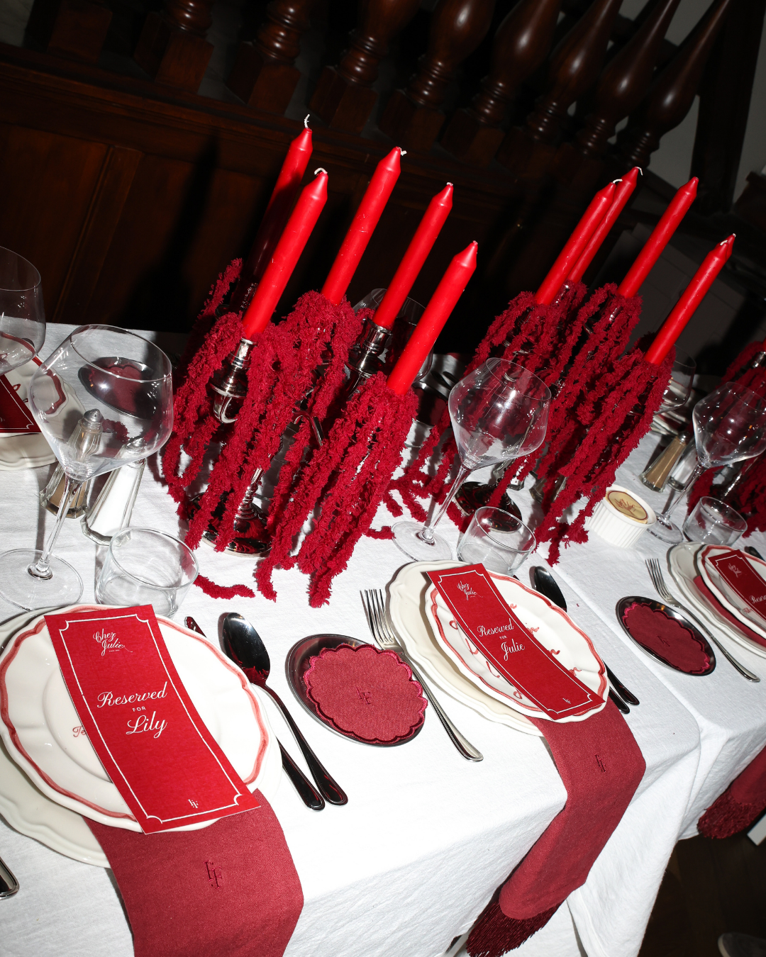 Chez Jules table styling by Imaginary Friends – red taper candles, scalloped plates, personalized place cards and deep red linen on a white tablecloth.