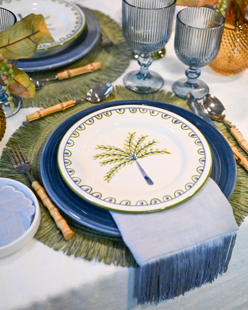 Close-up of Isla Bonita table styling – palm-tree plate, blue ceramic plates, bamboo cutlery and green raffia placemat by Imaginary Friends.